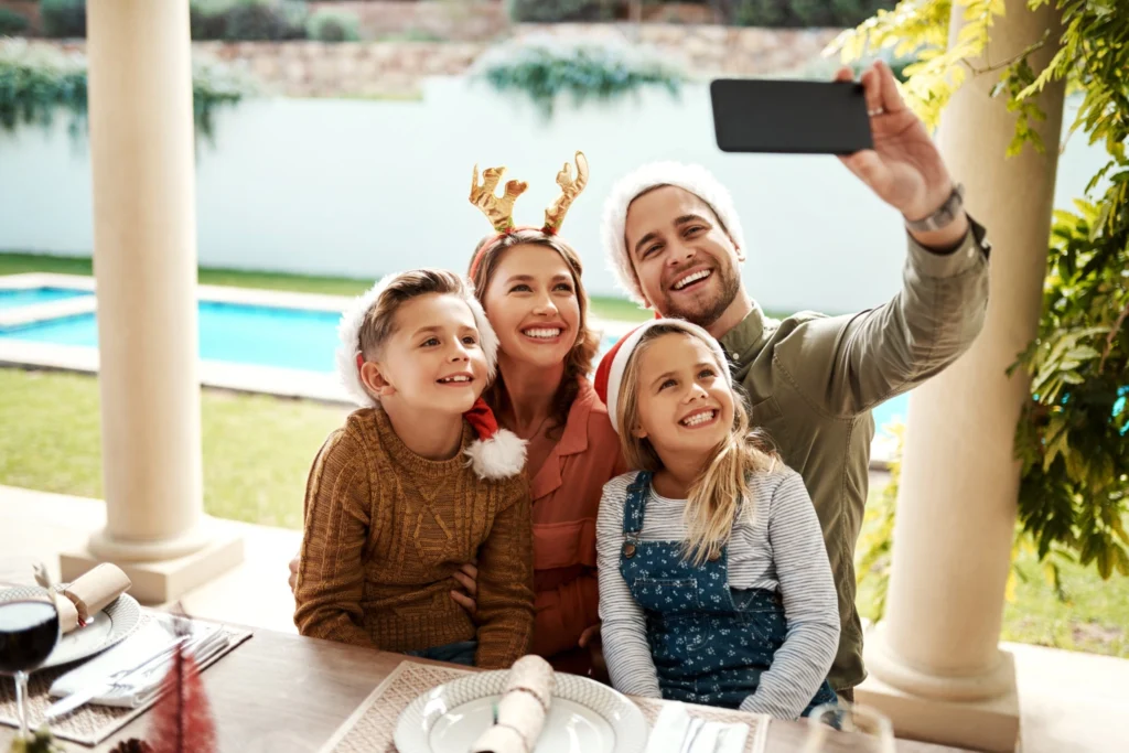 Pai segurando celular para selfie na mesa de ceia para o natal na piscina em família