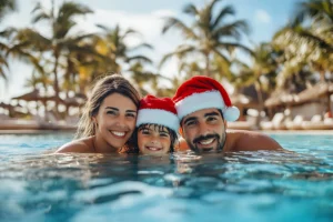 Família feliz comemorando o Natal na piscina com chapéus de Papai Noel e palmeiras ao fundo.