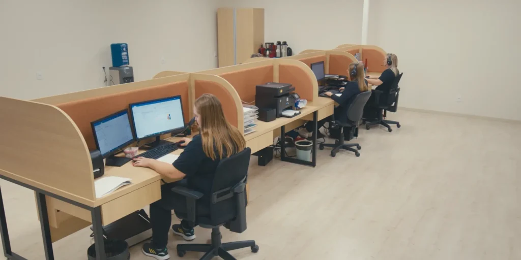 Equipe da Tholz atuando em estações de atendimento e suporte, com colaboradores trabalhando em computadores em ambiente corporativo organizado.