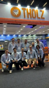 Equipe da Tholz reunida em estande de feira, com logotipo da marca em destaque e apresentação de soluções de automação, iluminação e aquecimento para piscinas.