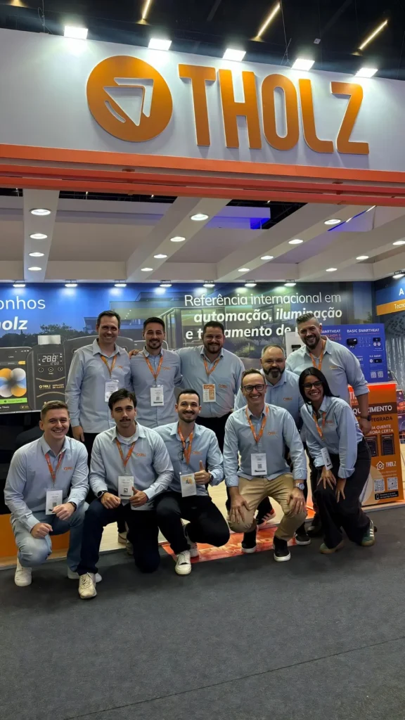 Equipe da Tholz reunida em estande de feira, com logotipo da marca em destaque e apresentação de soluções de automação, iluminação e aquecimento para piscinas.